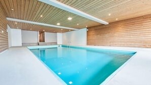 An indoor swimming pool with a wooden ceiling and walls, a clear blue pool, and a white floor.