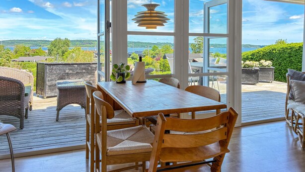 An open deck with a wooden table and chairs, a hanging light fixture, and a view of a green landscape through large windows. - Nice home in Børkop with WiFi (Børkop)