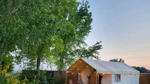 A tent-style accommodation with a patio area, surrounded by greenery and a wooden fence.