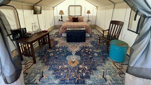 A tented room with a bed, two chairs, a desk, a lamp, and a rug.