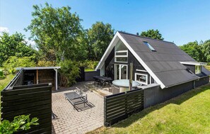 Een modern huis met een schuin dak, een terras met tafel en stoelen, en een omheind gazon.