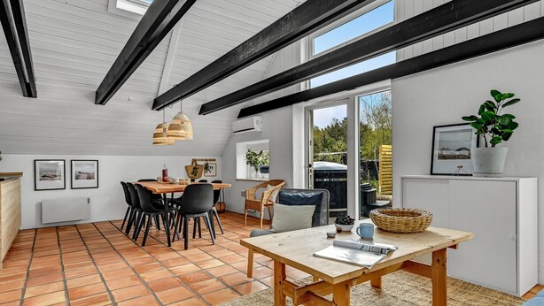 Un coin repas avec une table en bois, des chaises noires et un tapis tissé. Une fenêtre offre une vue sur la verdure à l’extérieur.