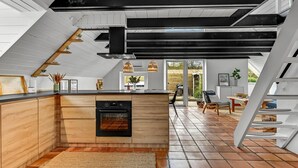 Une cuisine moderne dotée d’un îlot central, d’un four encastré et de luminaires suspendus.