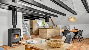 Une cuisine moderne dotée d’un poêle à bois, un coin repas avec une table et des chaises en bois, et un escalier menant à un niveau supérieur.