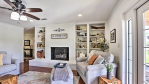 A living room with a fireplace, a ceiling fan, and a bookshelf. - Sunny Florida Abode - Patio, Pool, & Fire Pit (Marianna)