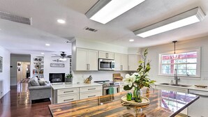 A modern kitchen with white cabinets, stainless steel appliances, and a wooden dining table with a vase of flowers. - Sunny Florida Abode - Patio, Pool, & Fire Pit (Marianna)