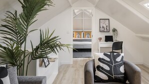 A modern loft bedroom with a sloped ceiling, a bed with a white and gray duvet, a desk with a computer, and a large plant. - Family holidays in Madeira - Casa da Lombada (Funchal)