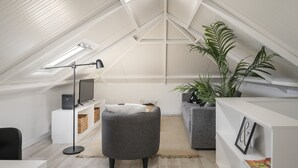 A modern loft bedroom with a sloped ceiling, built-in shelving, a grey sofa, a round ottoman, a TV, and a potted plant. - Family holidays in Madeira - Casa da Lombada (Funchal)