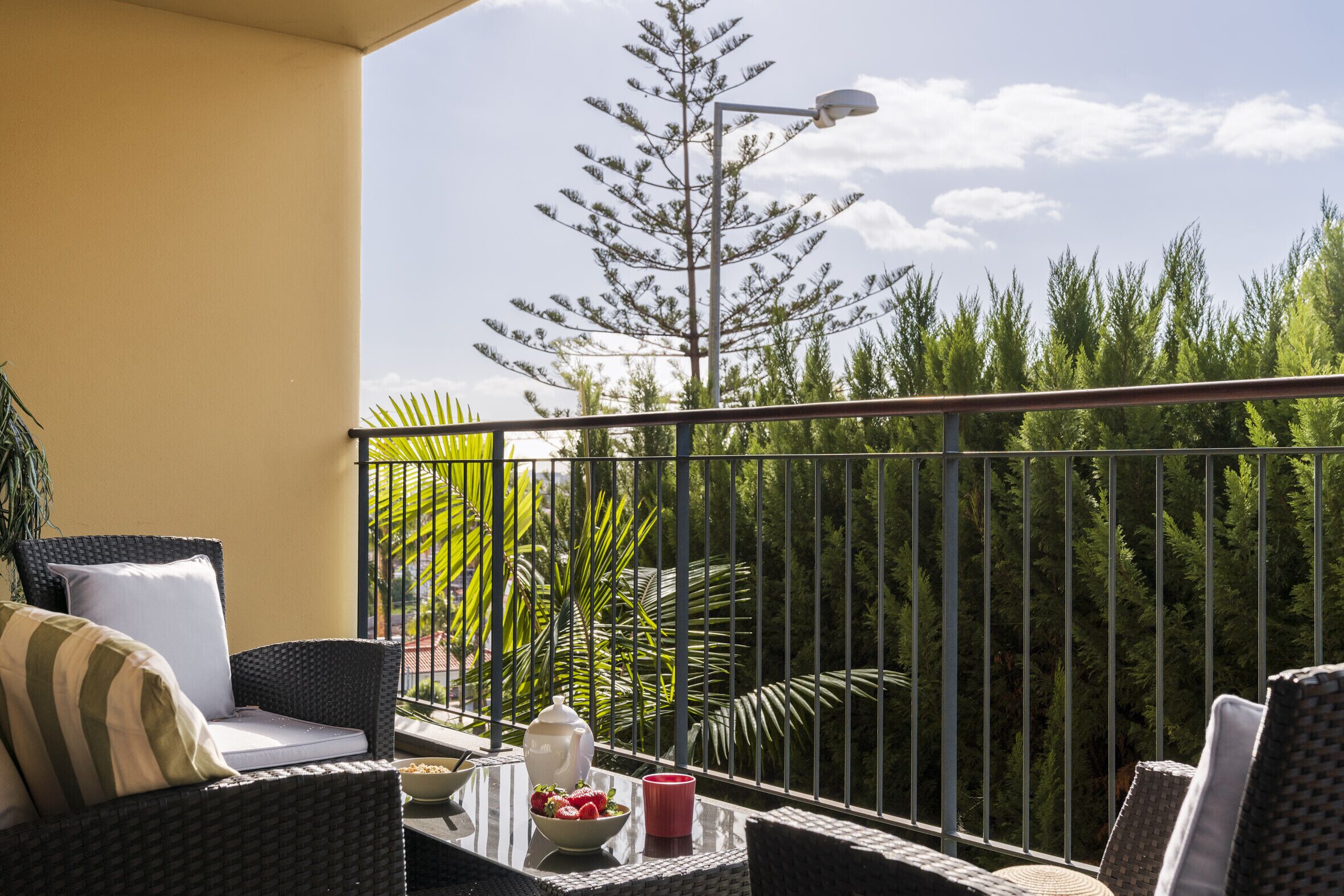 A balcony with wicker furniture, a table with a bowl of strawberries, a red cup, and a white vase.