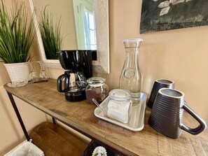 Un comptoir de cuisine avec une machine à café, des bocaux en verre, un pichet et un plateau sur lequel se trouve une tasse.
