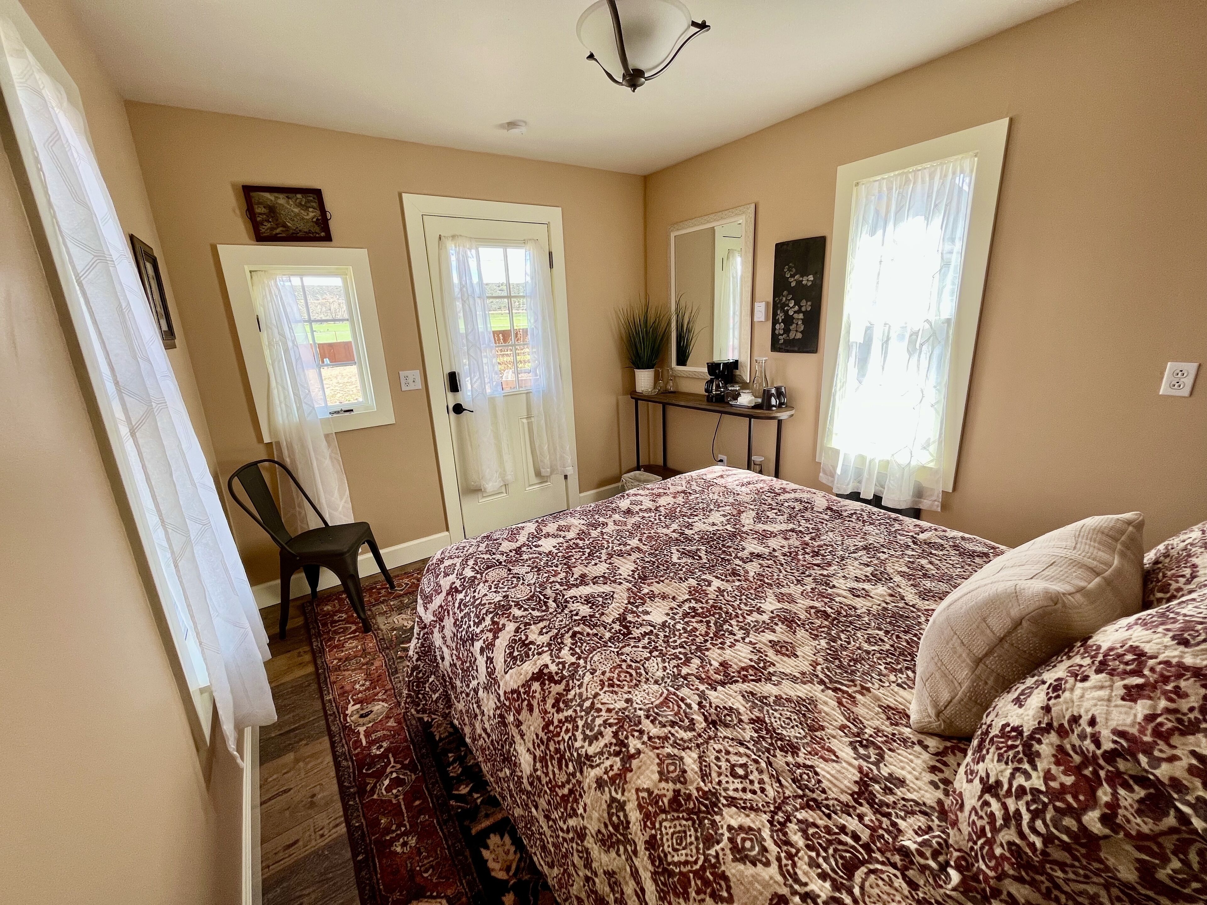 A bedroom with a large bed, a chair, a desk with a mirror, and two doors.