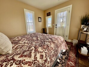 Une chambre à coucher avec un grand lit, deux portes, une chaise, une petite table avec une plante et un tapis.