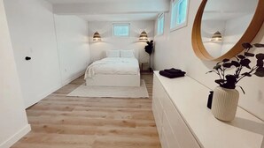 A bedroom with a bed, a dresser, a mirror, and a potted plant. - The California Suite (Fort St. John)