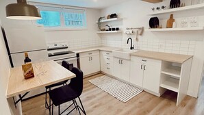 A modern kitchen with white cabinetry, a wooden dining table, and a black chair. - The California Suite (Fort St. John)
