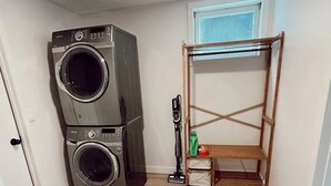 A laundry room with two stacked washing machines, a wooden drying rack, and a vacuum cleaner. - The California Suite (Fort St. John)
