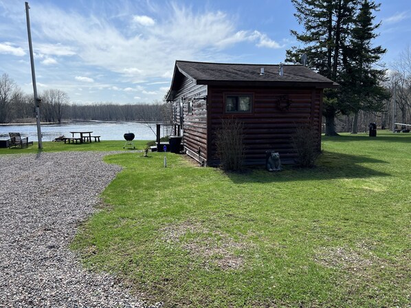A small wooden cabin with a porch, a picnic table, and a grill, located near a body of water. - EAGLE LODGE - Cozy Cabin Overlooking the Beautiful E. Fork of the Chippewa River (Loretta)