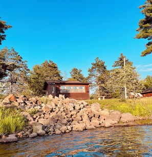 A cabin with a wooden exterior, a window, and a small porch area. - EAGLE LODGE - Cozy Cabin Overlooking the Beautiful E. Fork of the Chippewa River (Loretta)