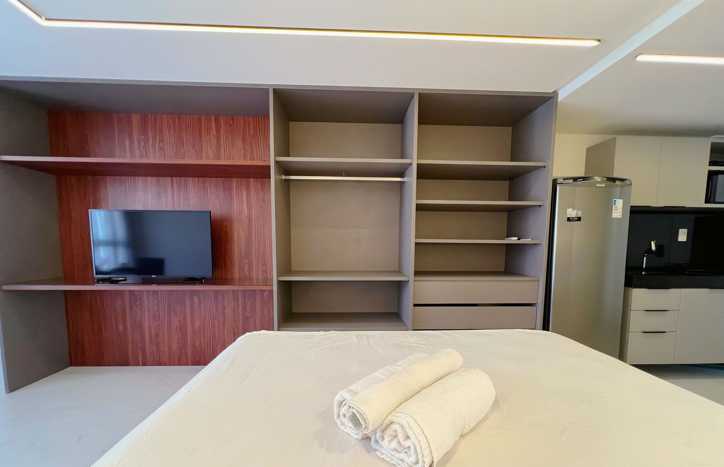 A modern hotel room with a flat-screen TV, built-in wardrobe, and a kitchenette.