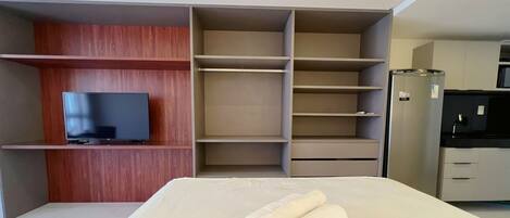 A modern hotel room with a flat-screen TV, built-in wardrobe, and a kitchenette.