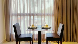 Uma área de refeições com uma mesa posta para dois, duas cadeiras e vista através de cortinas leves.
