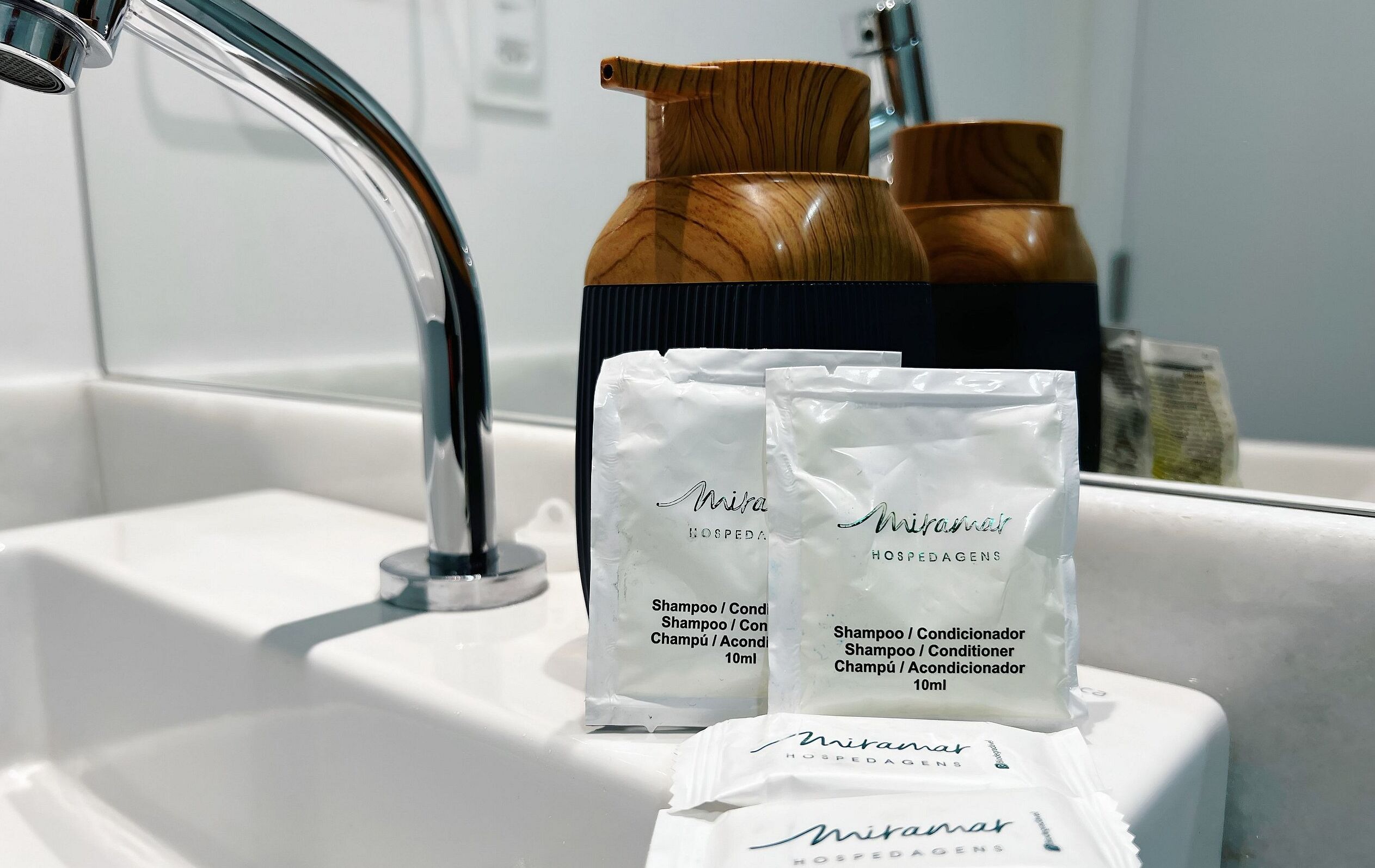 A bathroom sink with two wooden shampoo bottles and three white sachets of shampoo.