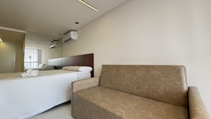 Quarto de hotel moderno com cama, sofá, espelho grande e aparelho de ar condicionado.