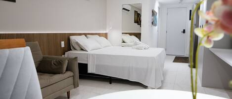 A modern hotel room with a bed, a sofa, a small table, and an air conditioning unit.