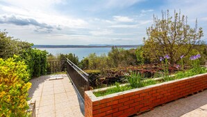 Terraço com vista para um lago e montanhas ao longe, cercado por vegetação e um muro de tijolos.