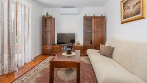 Uma sala de estar com televisão, armários de madeira, sofá e tapete estampado.