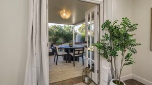 Uma porta dá acesso a um pátio externo com mesa e cadeiras, um vaso de planta e um lustre.