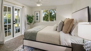 Quarto com cama, ventilador de teto, janela e porta que dá para uma varanda.