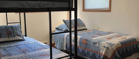 Une chambre avec des lits superposés, un ventilateur de plafond, une fenêtre avec des stores et un plancher en bois.