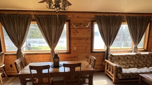 A cozy cabin interior with a wooden dining table, chairs, a sofa, and curtains over windows. - EAGLE LODGE - Large log cabin on the E. Fork of Chippewa River (Loretta)