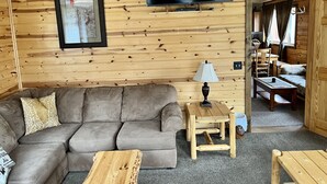A cozy cabin interior with a wooden wall, a flat-screen TV, a sofa, a coffee table, and a dining area. - EAGLE LODGE - Large log cabin on the E. Fork of Chippewa River (Loretta)