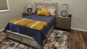 Ein Schlafzimmer mit Bett, Nachttischen, einem hölzernen Kopfteil, einem Teppich und Wanddekorationen.