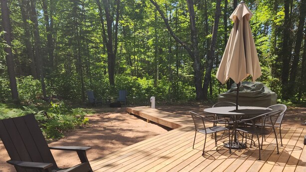 Eine Holzterrasse mit Gartenmöbeln, darunter Stühle und ein Tisch, umgeben von einem bewaldeten Gebiet.