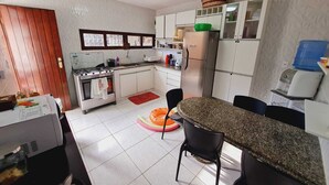 Une cuisine compacte avec des meubles blancs, un réfrigérateur en acier inoxydable et un coin repas doté d’un comptoir en granit et de chaises noires.