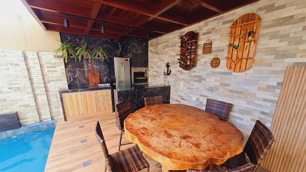 Un espace extérieur aménagé pour les repas, avec une piscine, des meubles en bois et un mur en pierre agrémenté d’étagères à vin.