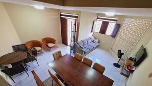 Un vaste espace de vie comprenant une grande table à manger en bois, deux canapés et un téléviseur fixé au mur.