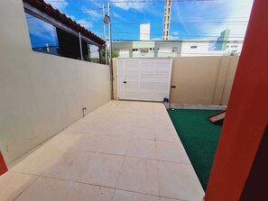 Un petit patio clos, doté d’un sol carrelé, d’une zone recouverte de gazon synthétique et d’une porte blanche.