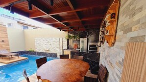 Un espace extérieur avec piscine, aménagé avec un coin repas comprenant une table ronde et des chaises en osier.