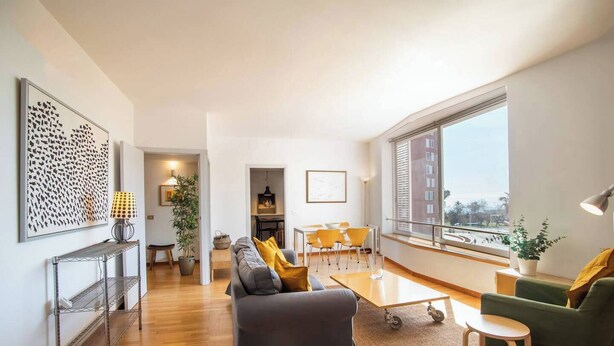 Una sala moderna con un sofá gris, un sillón verde y una zona de comedor con sillas amarillas.