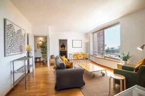 Una sala moderna con un sofá gris, un sillón verde y una zona de comedor con sillas amarillas.
