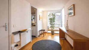 Un pasillo con piso de madera, un tapete redondo, una planta en maceta, un banco y una puerta que da a una zona de cocina.
