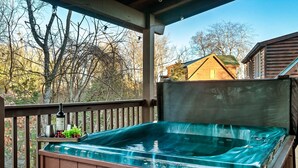 Un jacuzzi en una terraza de madera con vistas a árboles y una casa al fondo.