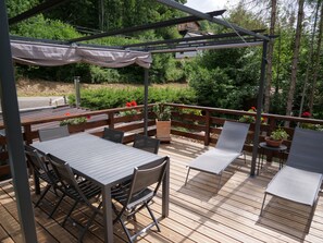 Eine Terrasse im Freien mit Holztischen und -stühlen, einer Pergola mit Dach und Kübelpflanzen.