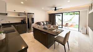 A modern kitchen with a central island, a dining area, and a sliding glass door leading to a patio with a hammock. - Lovely condo w/private pool, 3 min from the beach! (Playa del Carmen)