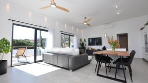 Een moderne woonkamer met een bank, eettafel, stoelen, plafondventilators en een televisie.