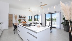 Een moderne keuken met een centraal eiland, een zithoek met tafel en stoelen, en een grote schuifpui die uitkomt op een balkon met uitzicht.