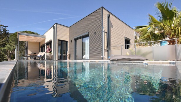 Een modern huis met een zwembad, grote ramen en een overdekt terras.